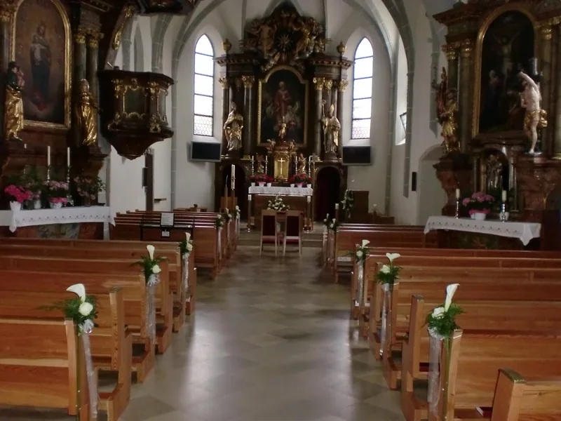 Kirchenbänke mit Blumenschmuck am Mittelgang, vorne der Altar