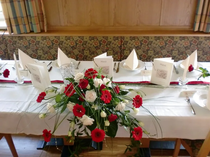 Hochzeitstafel mit rot-weißem Rosengesteck im Gasthaussaal
