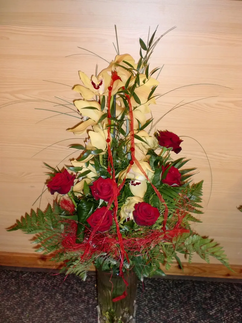 Hoher Strauß mit Orchideen, roten Rosen und Farn vor einer Holzwand