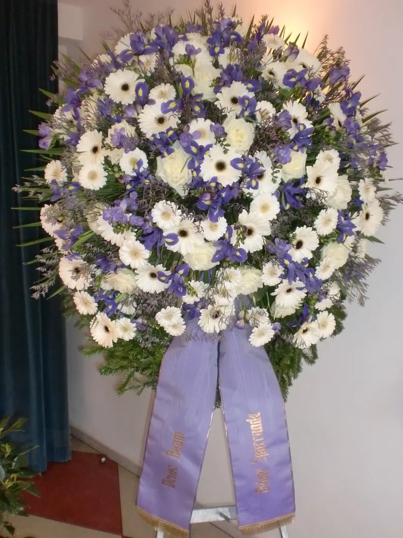 Kranz aus weißen Gerbera und blauen Blüten mit lila Schleife