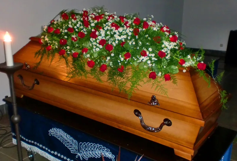 Sarggesteck aus roten Rosen und Schleierkraut auf einem Holzsarg